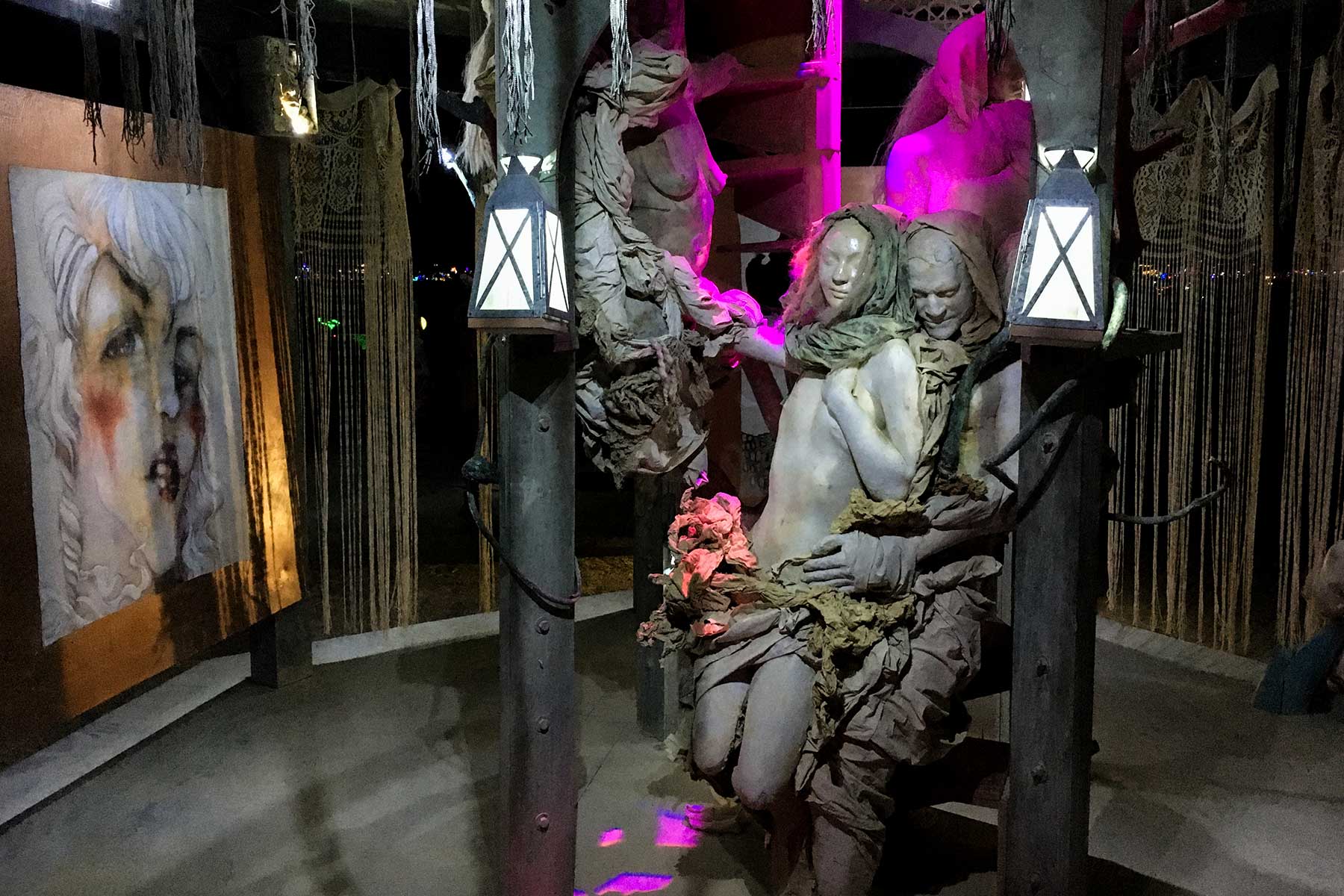 Inside the structure at night: the embracing pair between two lanterns, beside a portrait painting of a woman