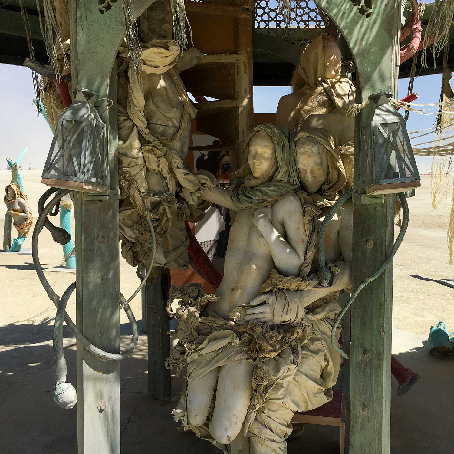 The embracing cast figures by day, framed by weathered green posts, hanging lanterns and draped cloth