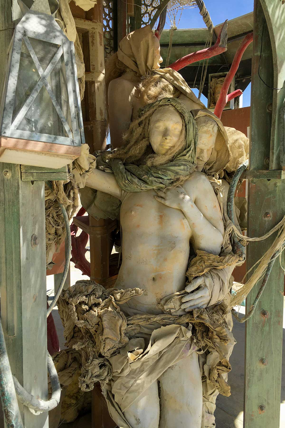 The embracing cast figures in daylight, the woman in a green scarf held from behind beside a hanging lantern