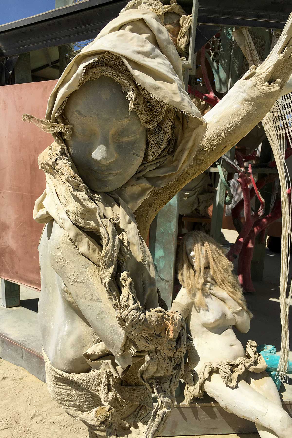 A hooded cast figure reaching up beside the structure, with a long-haired seated figure behind her